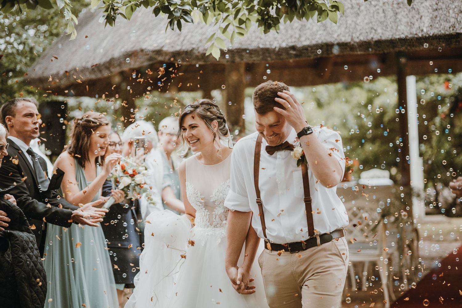 Joyful celebration as confetti falls during an outdoor wedding ceremony with attendants in mint green dresses.