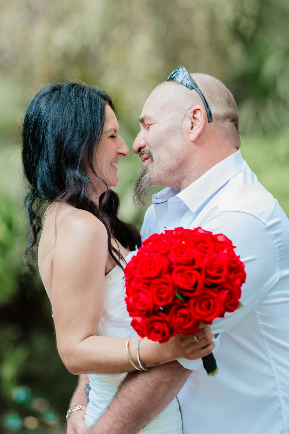 Romantic wedding couple shares an intimate moment outdoors with striking red roses.
