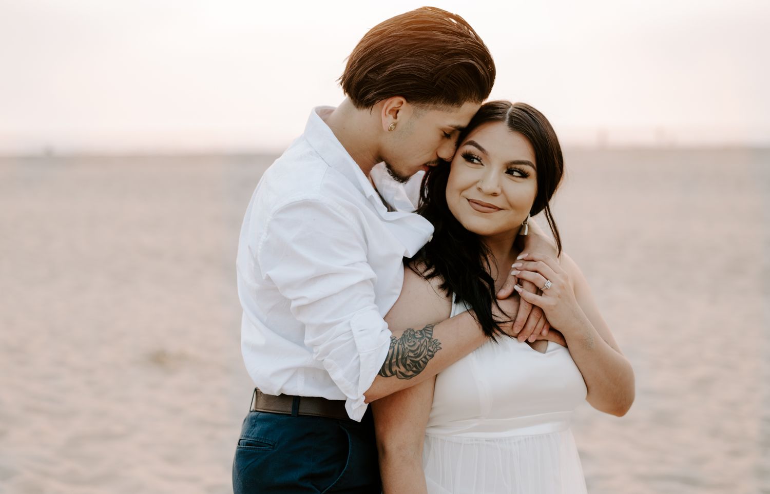 Romantic couple shares an intimate moment on a sandy beach at sunset.