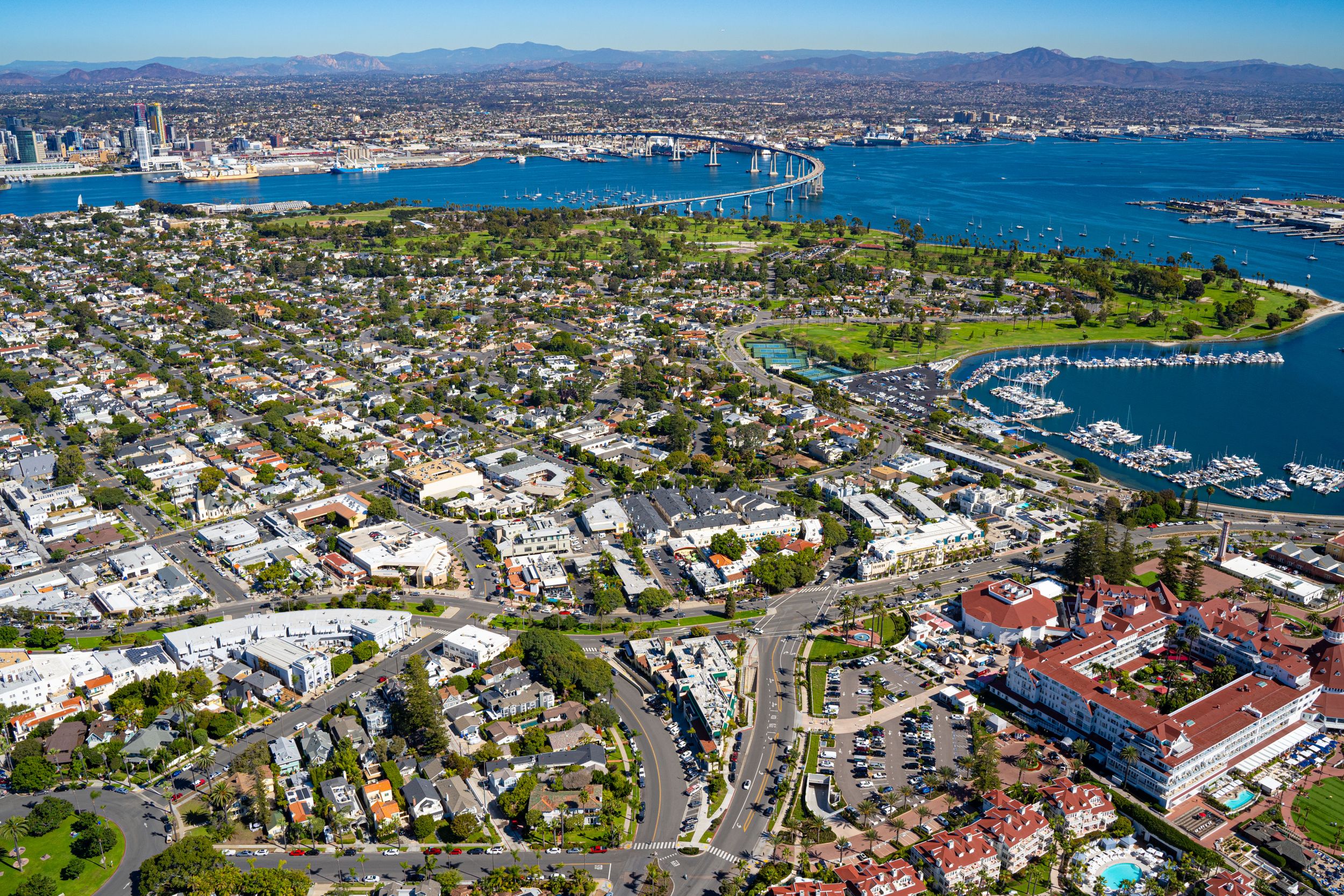 High-angle view of Coronado residential neighborhoods, green spaces, and the marina, looking across San Diego Bay toward the Coronado Bridge
