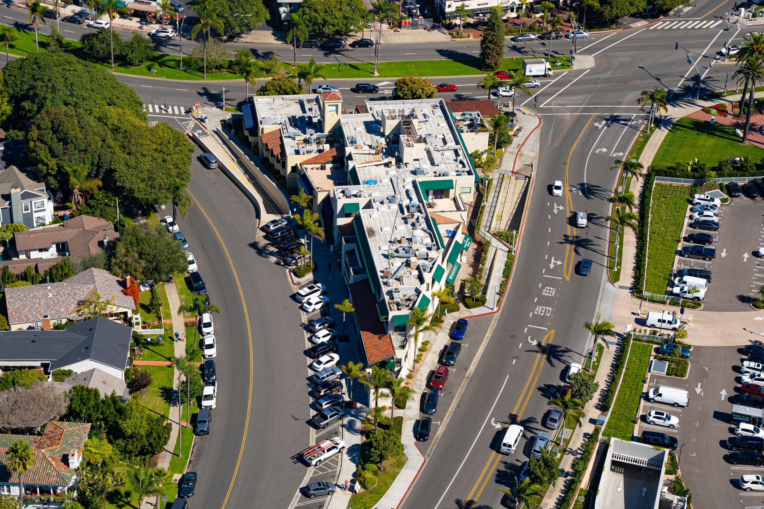 Top-down aerial view of a unique, wedge-shaped building situated at a Y-intersection between two curving streets with parked cars.