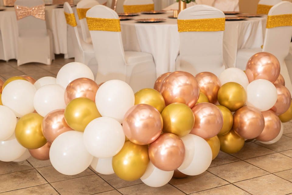 Pixs By Tina captures a festive balloon garland in gold, rose gold, and white colors decorates a floor space for an elegant party setup.