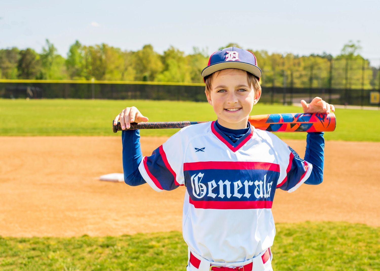 Young baseball player in Generals uniform poses with bat on baseball field.