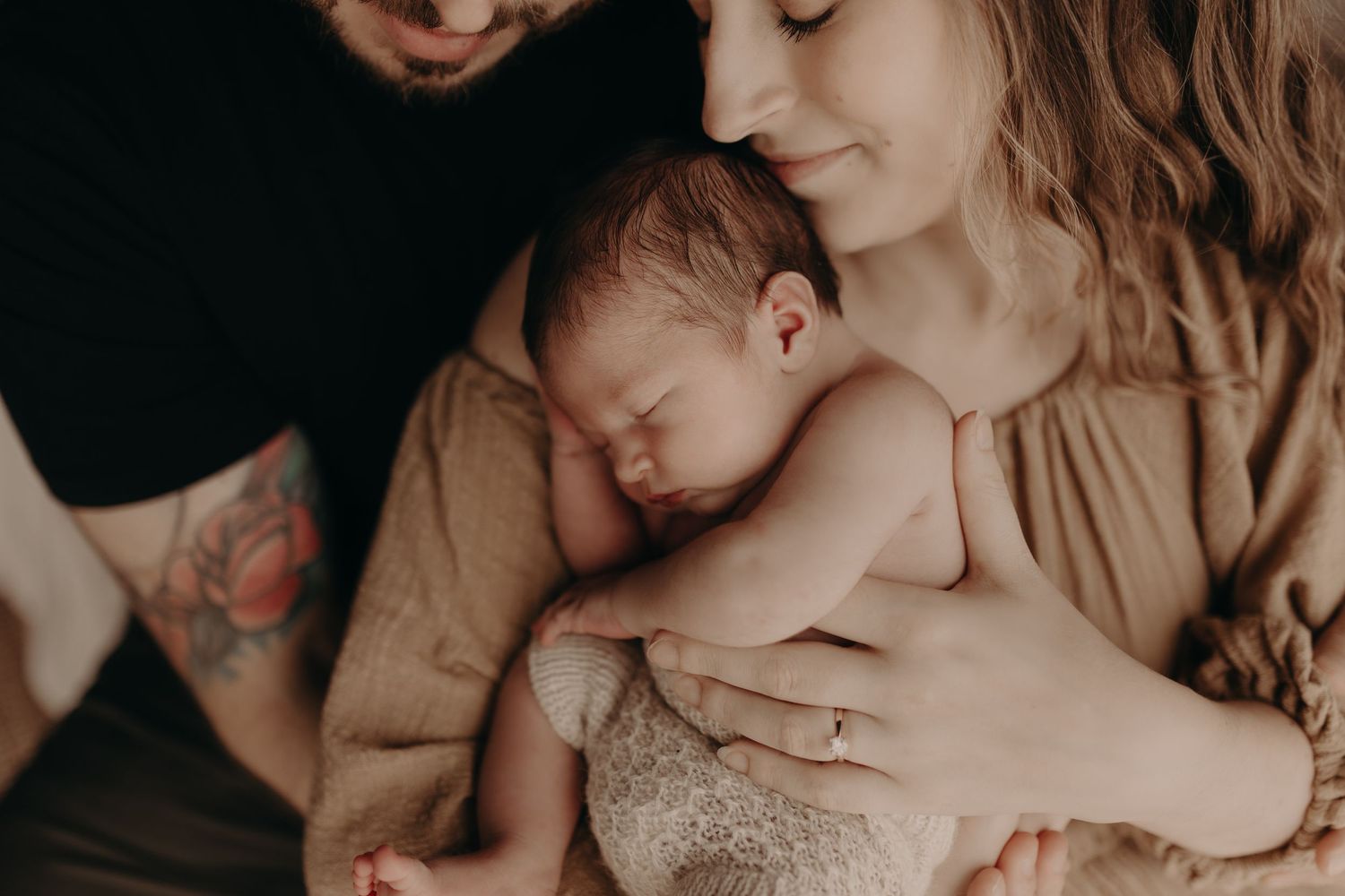 Intimate moment showing newborn baby being cradled in warm, neutral tones.