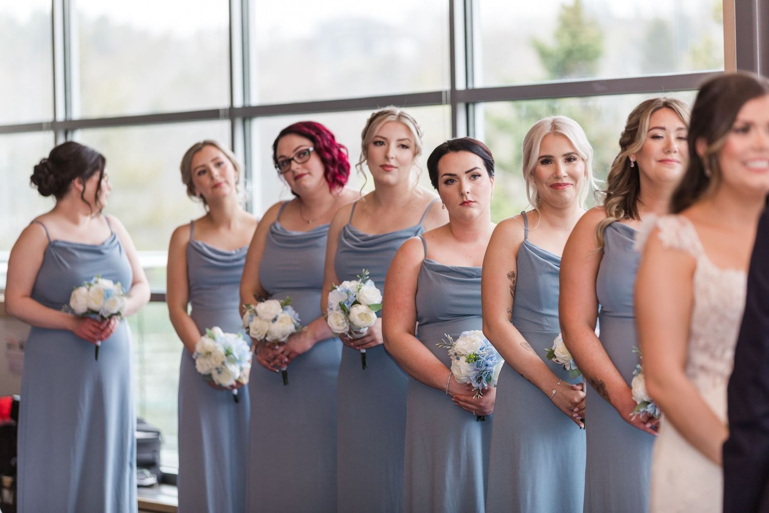 Bridesmaids wearing matching dusty blue dresses pose together holding white floral bouquets.