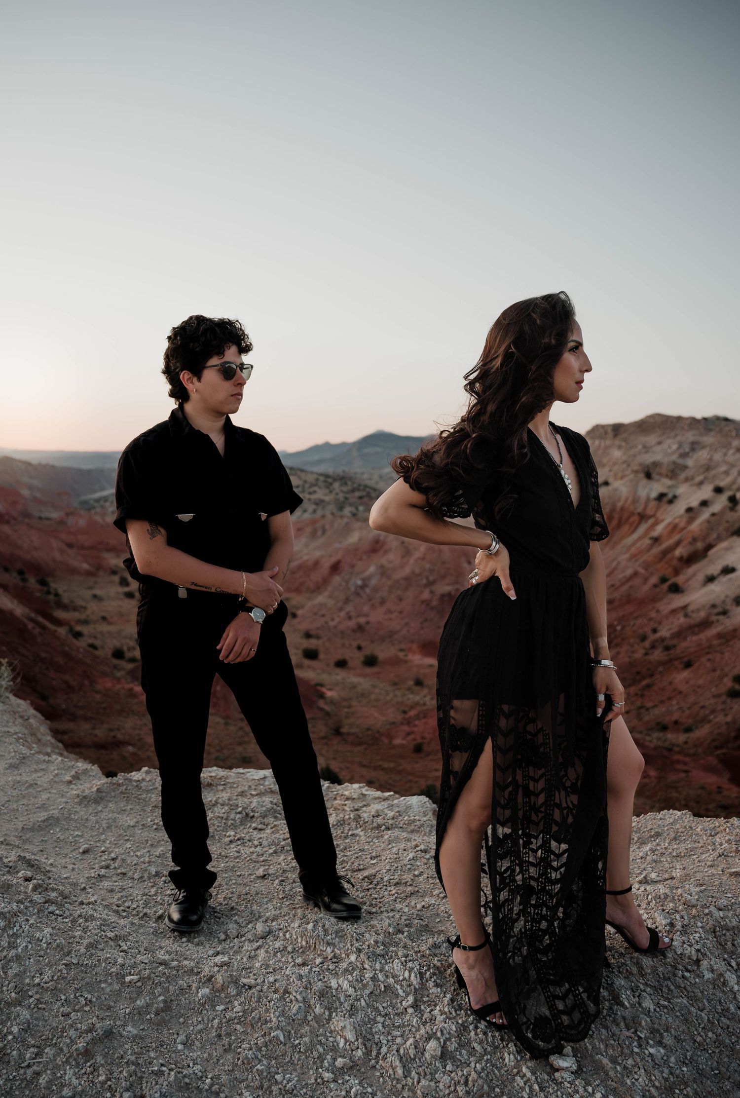 Stylish couple poses on rocky outcrop overlooking vast desert canyon.