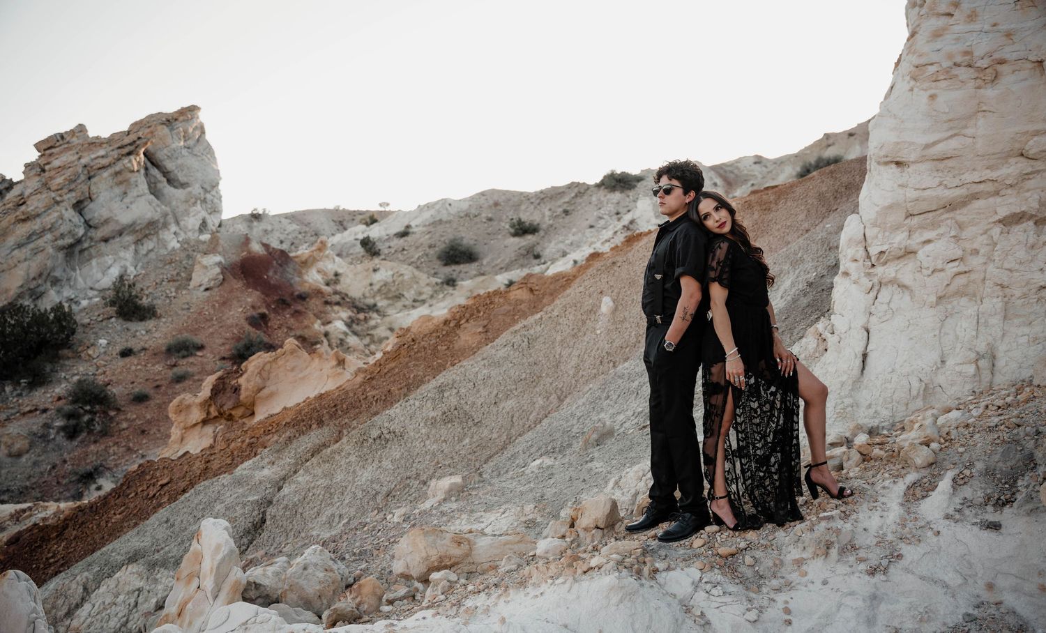 A couple embraces while standing on white rock formations in a desert landscape.