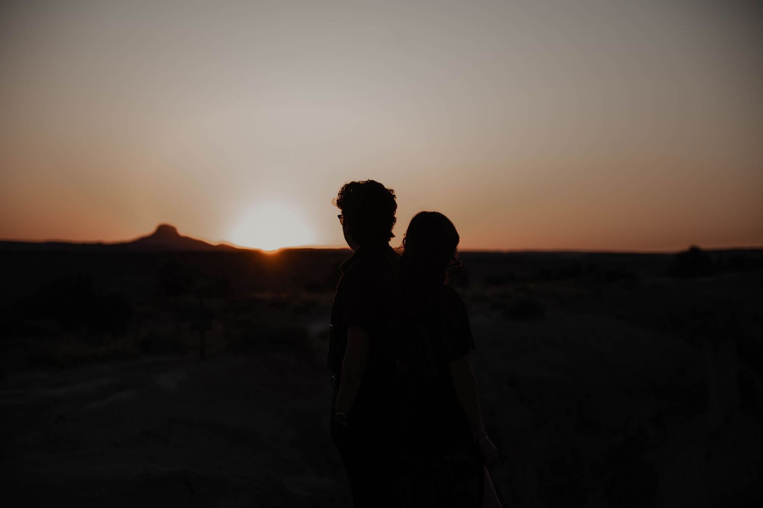 Two silhouettes stand together against a dramatic desert sunset.