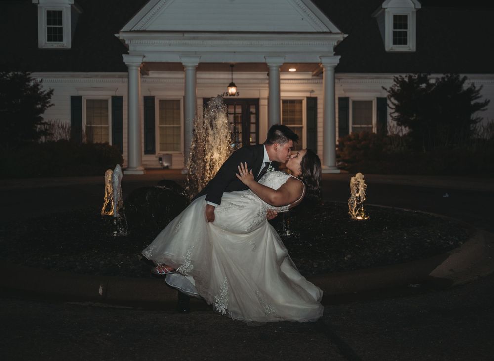 A dramatic nighttime wedding dip pose in front of an elegant white colonial house.