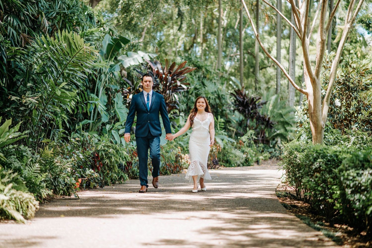 Couple walking hand in hand through a lush tropical garden pathway.