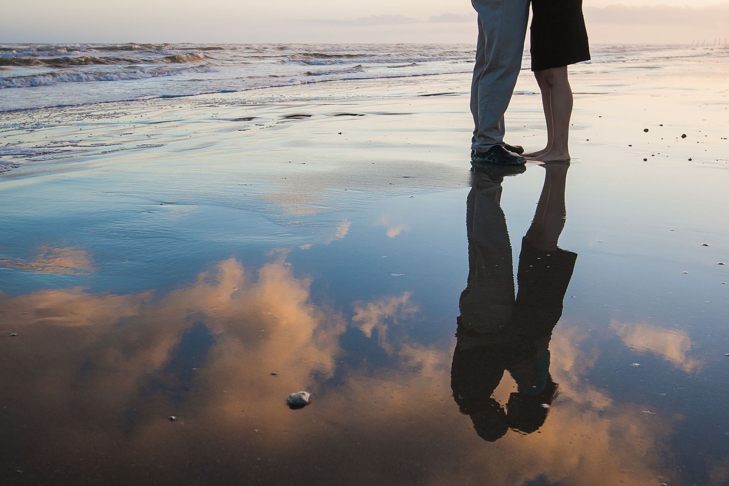 Silhouettes reflect in wet sand during sunset at the beach.
