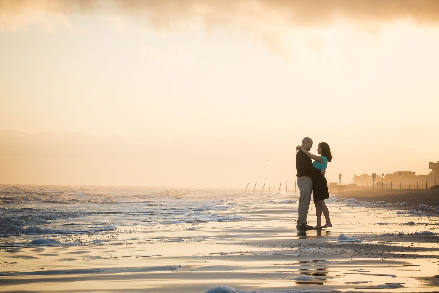 Silhouettes of people walking along a beach at sunset with orange sky reflections in the water.