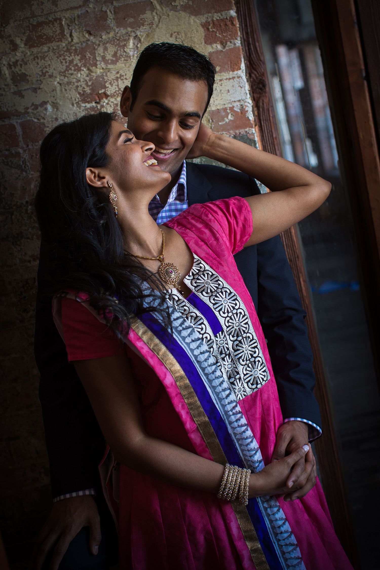 A couple shares an intimate moment against a rustic brick wall background.