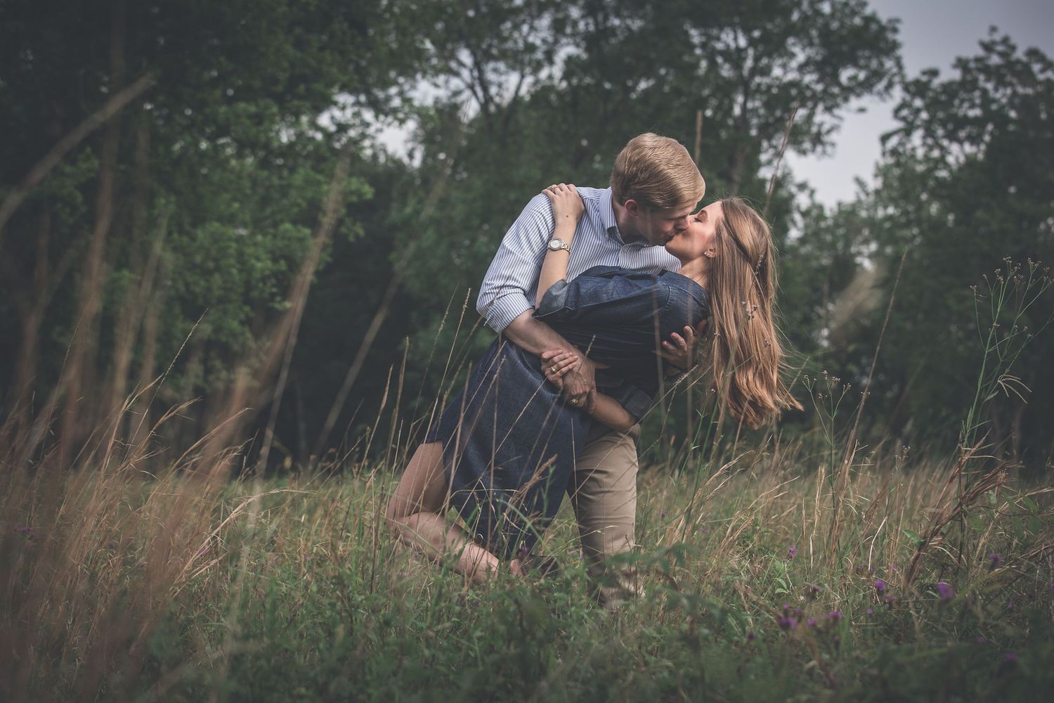 A couple sits close together in tall grass during an outdoor photo session.
