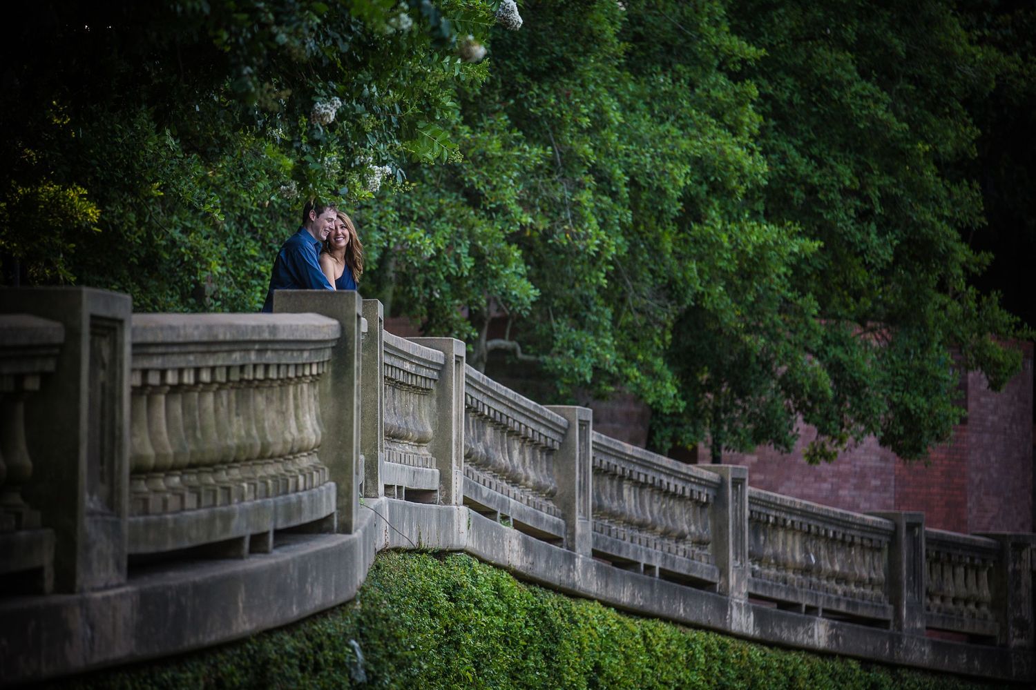 Romantic couple sharing an intimate moment on a stone bridge surrounded by lush greenery.