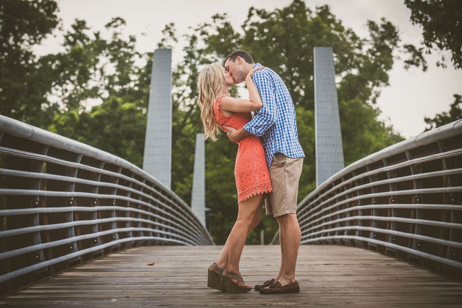 Couple embracing on a modern metal bridge during a golden hour photoshoot.