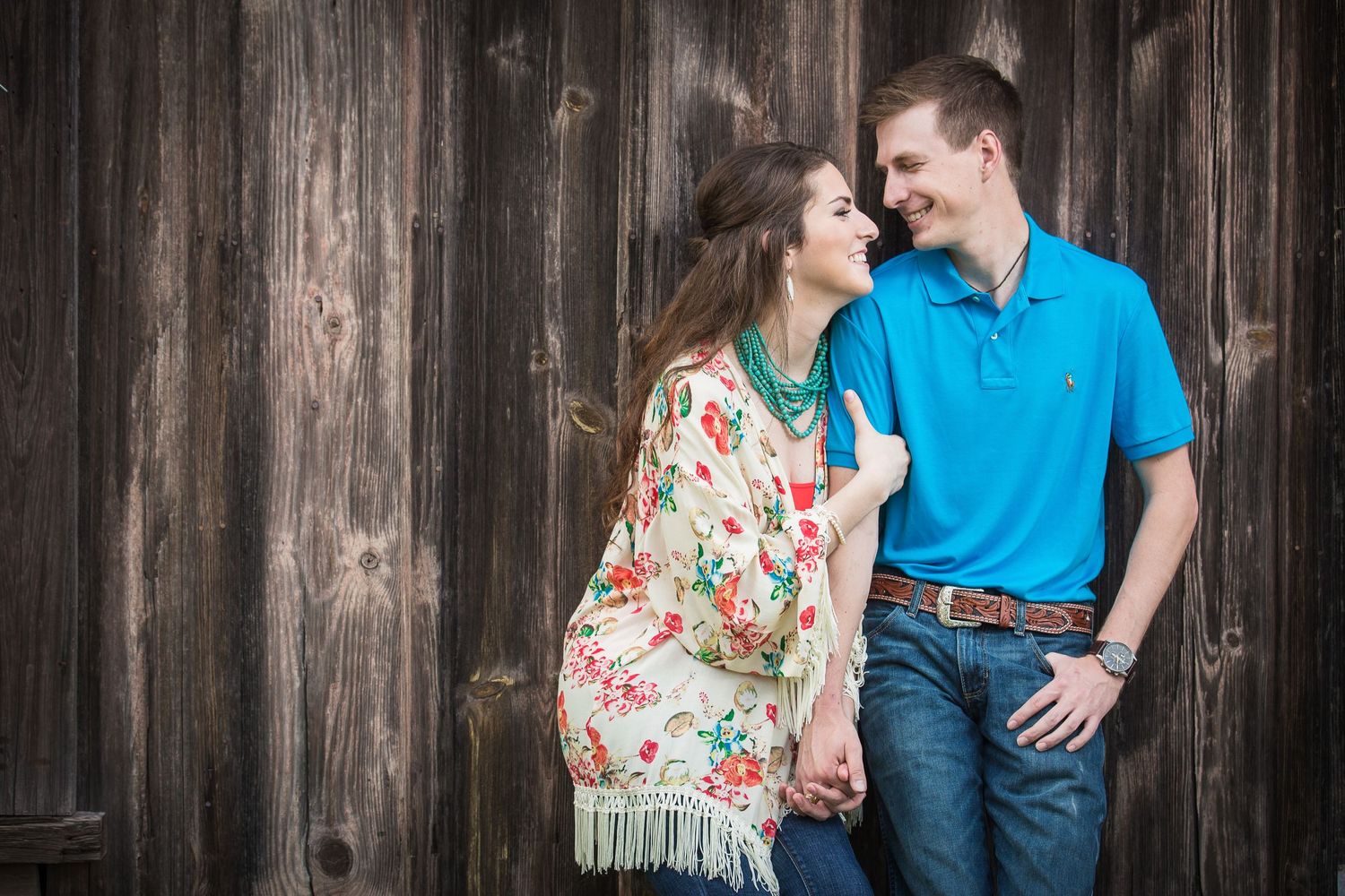 Couple poses against rustic wooden wall backdrop during engagement session.