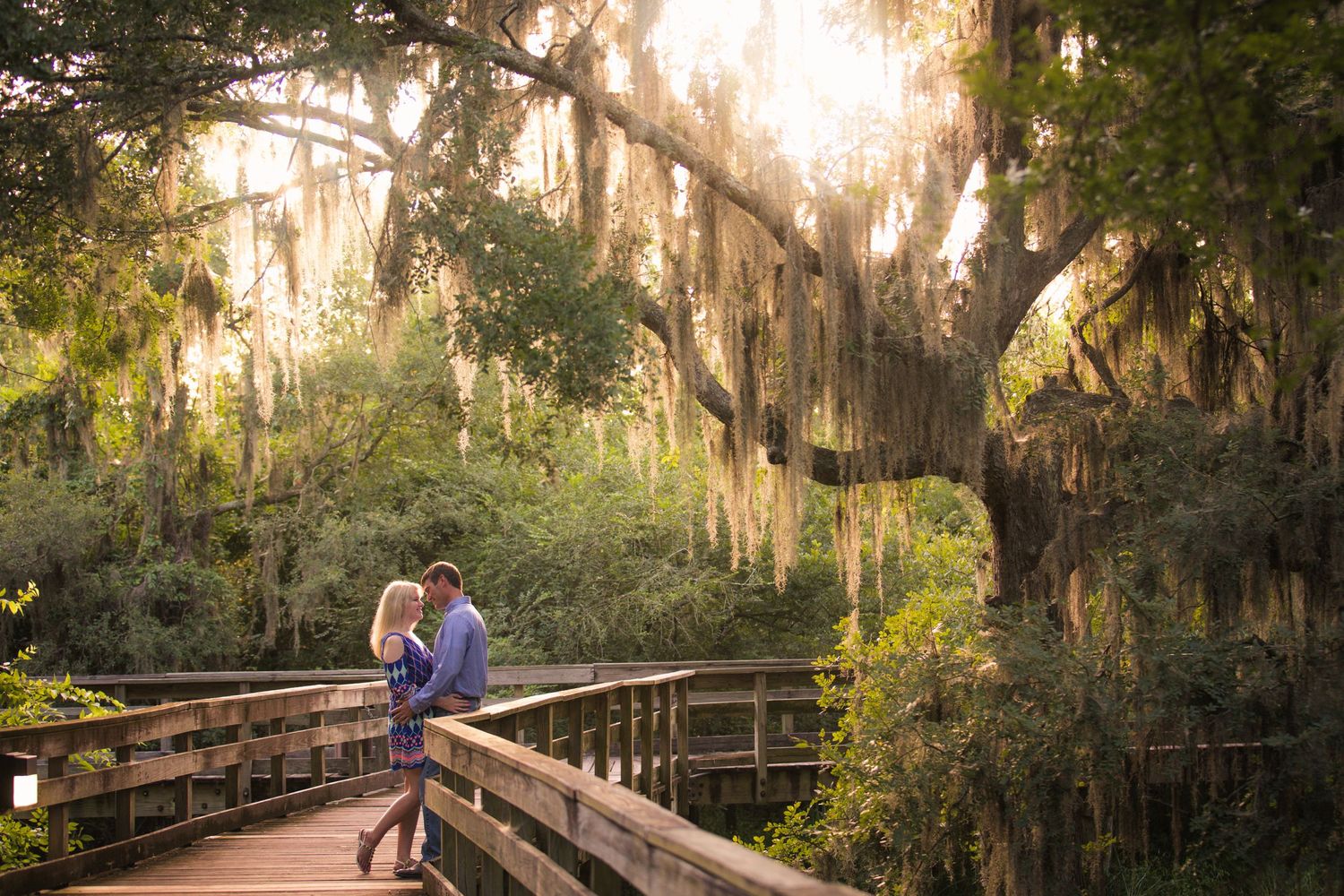 Romantic boardwalk engagement photos in a mossy Southern garden at golden hour.