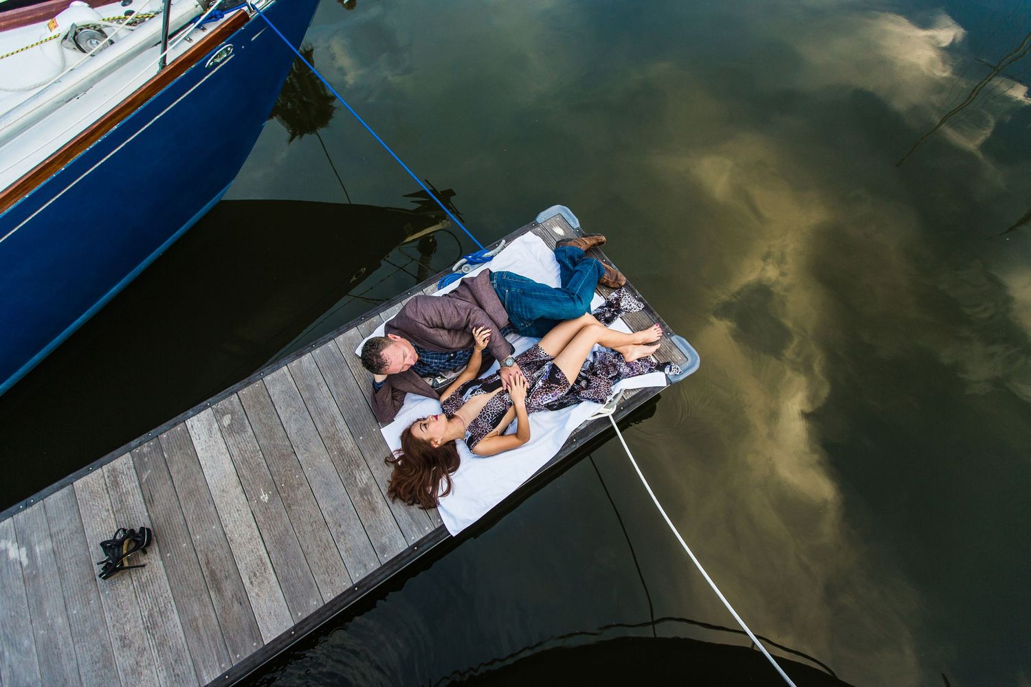 Couple lounges on wooden dock over reflective water at sunset.