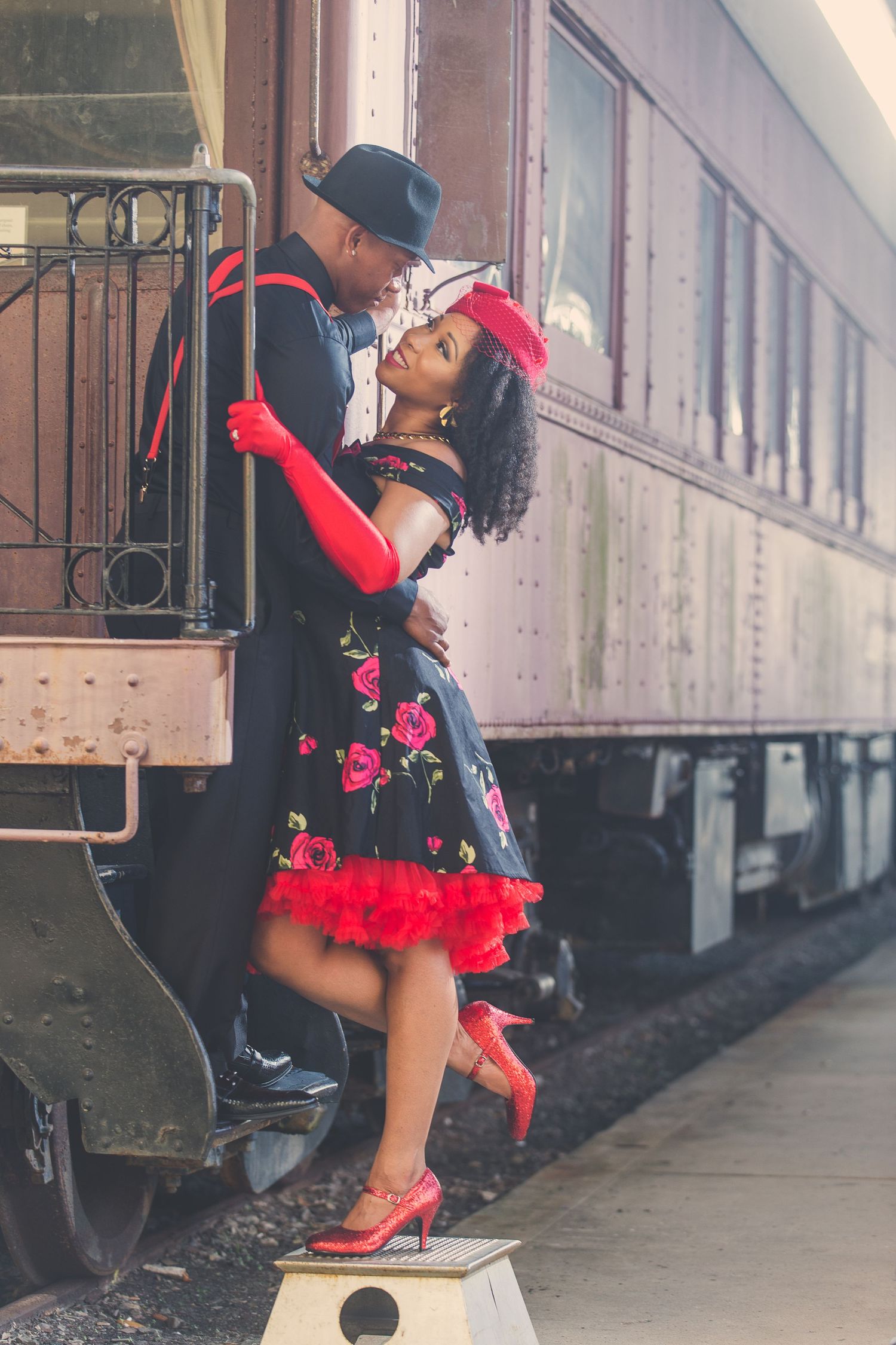 Vintage train car photoshoot featuring red dress and dramatic poses against classic railway backdrop.