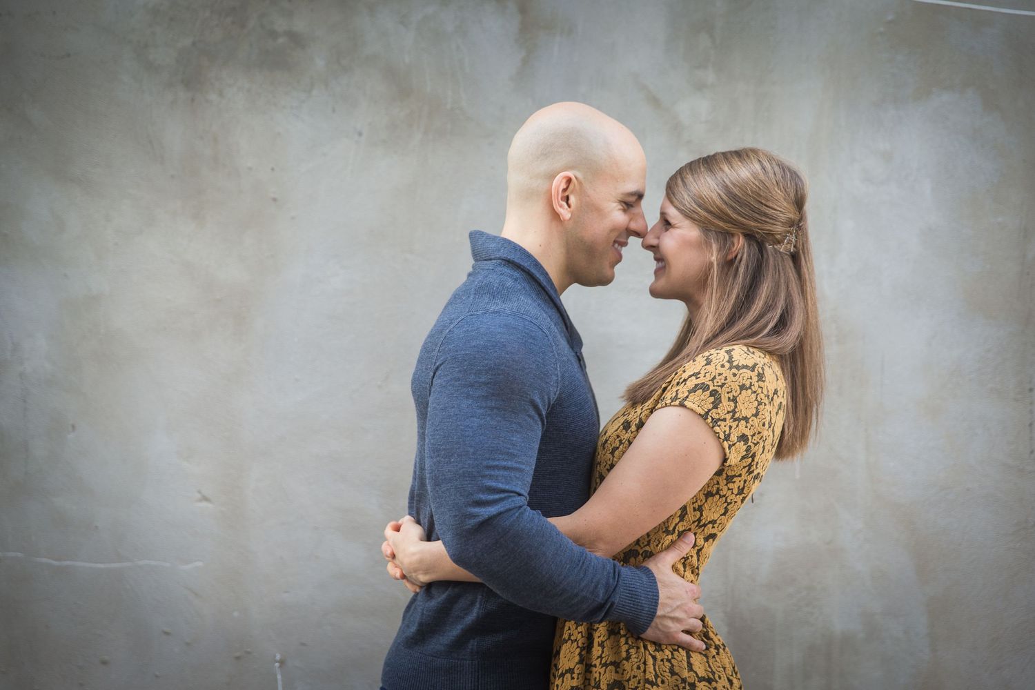Intimate portrait session against textured gray wall with moody lighting.