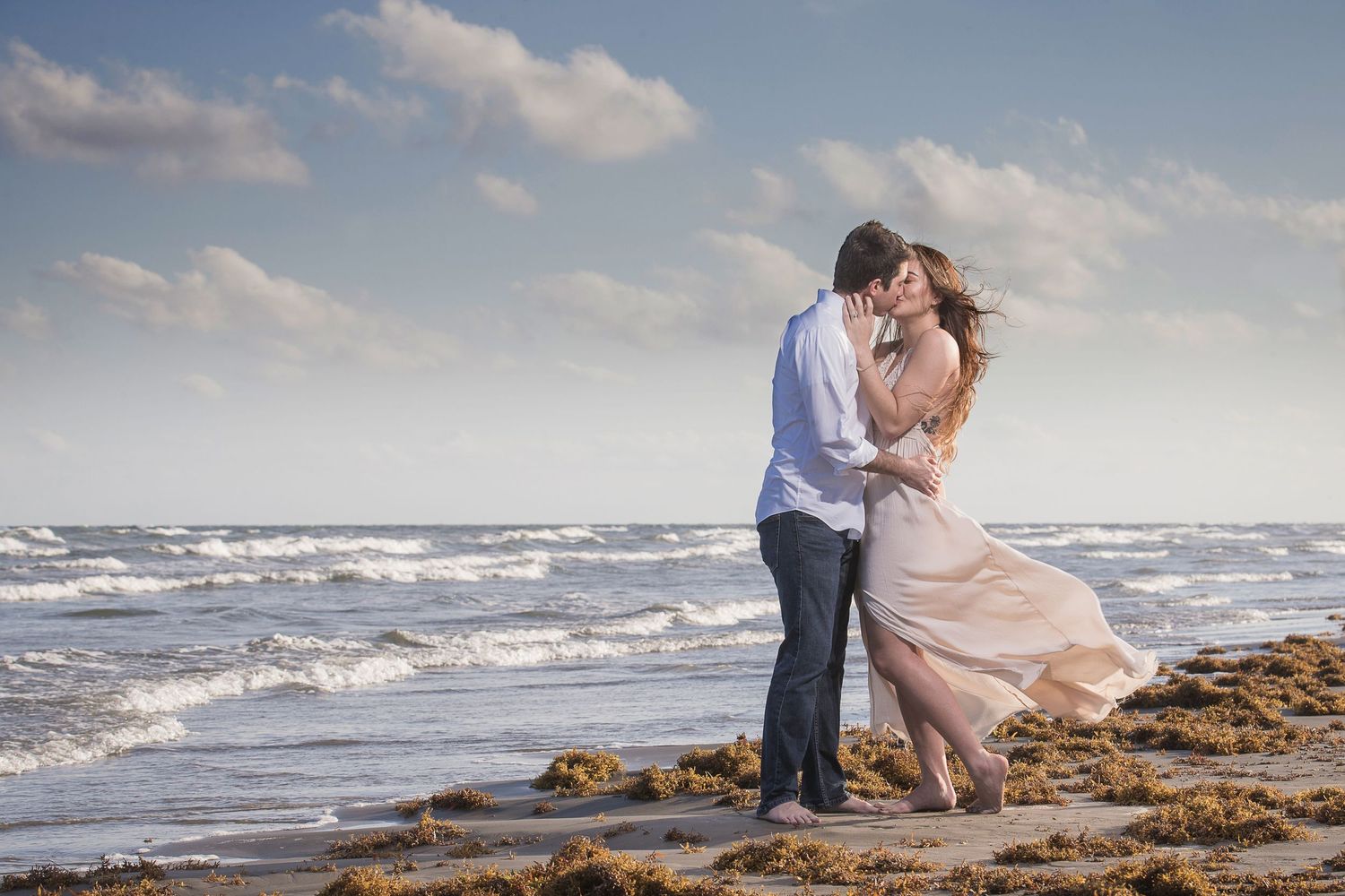Romantic beach photoshoot with crashing waves and cloudy skies in the background.