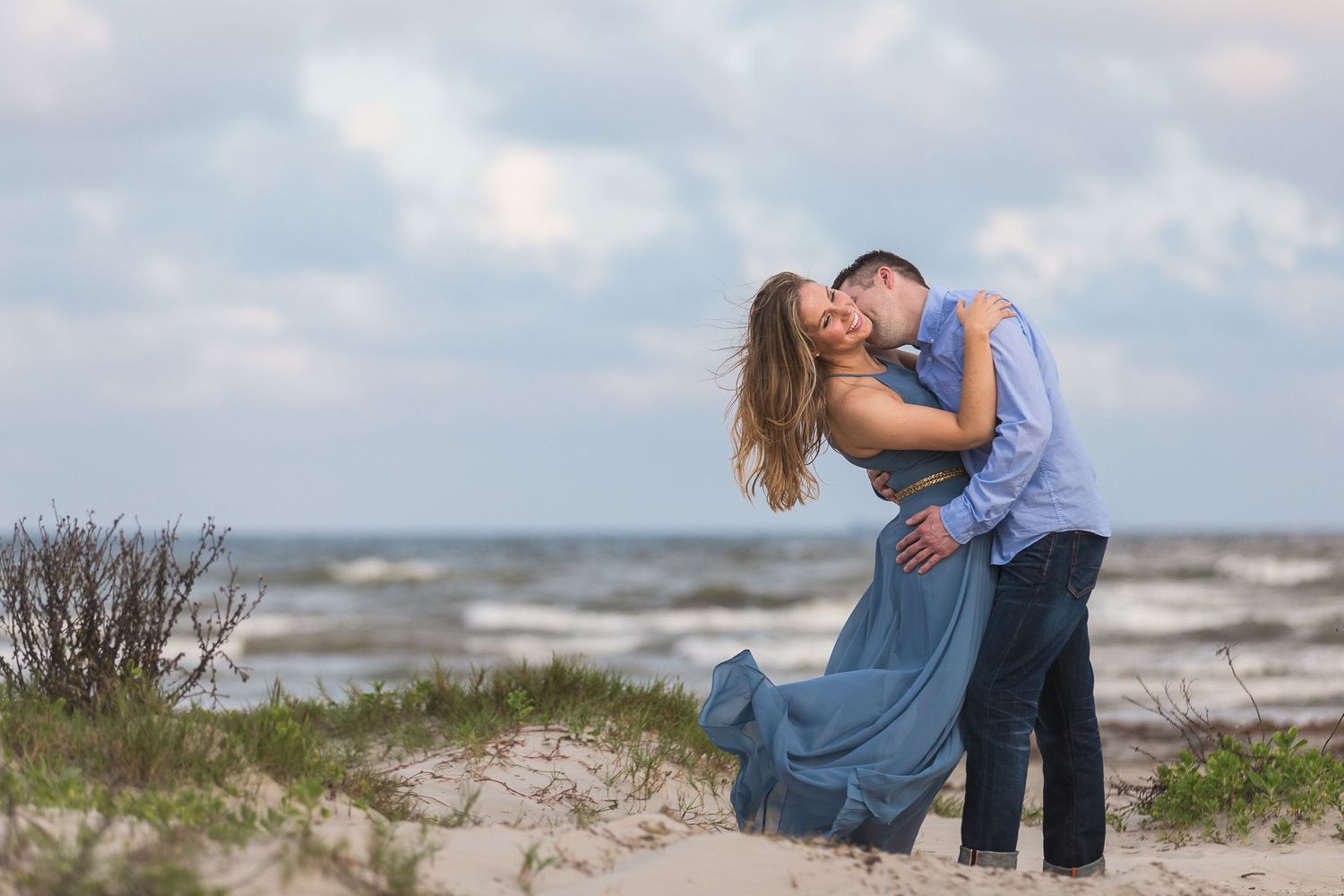 Couple shares intimate moments along a windswept beach shoreline.