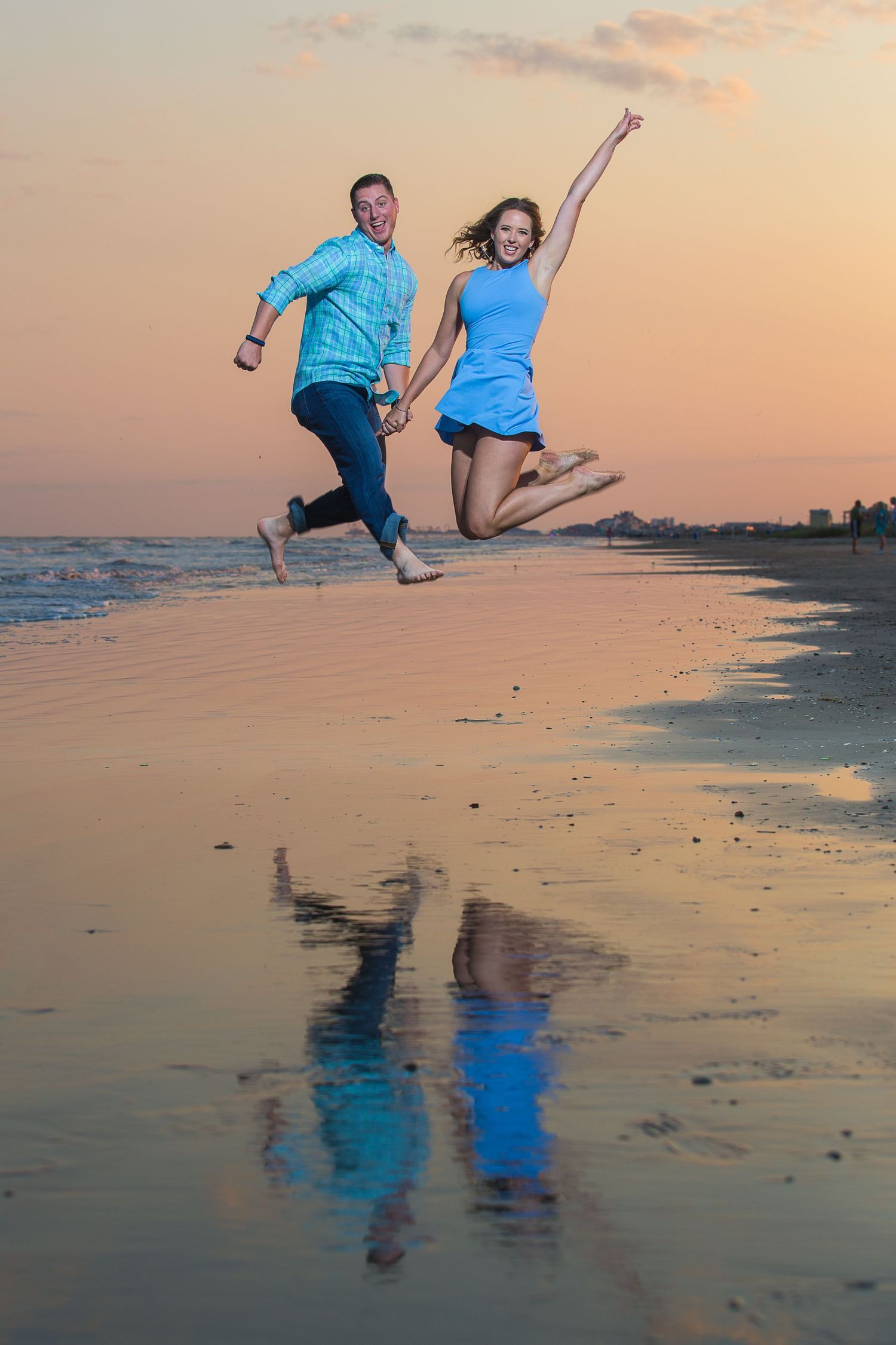 Playful couple jumping and reflecting in wet beach sand during sunset.