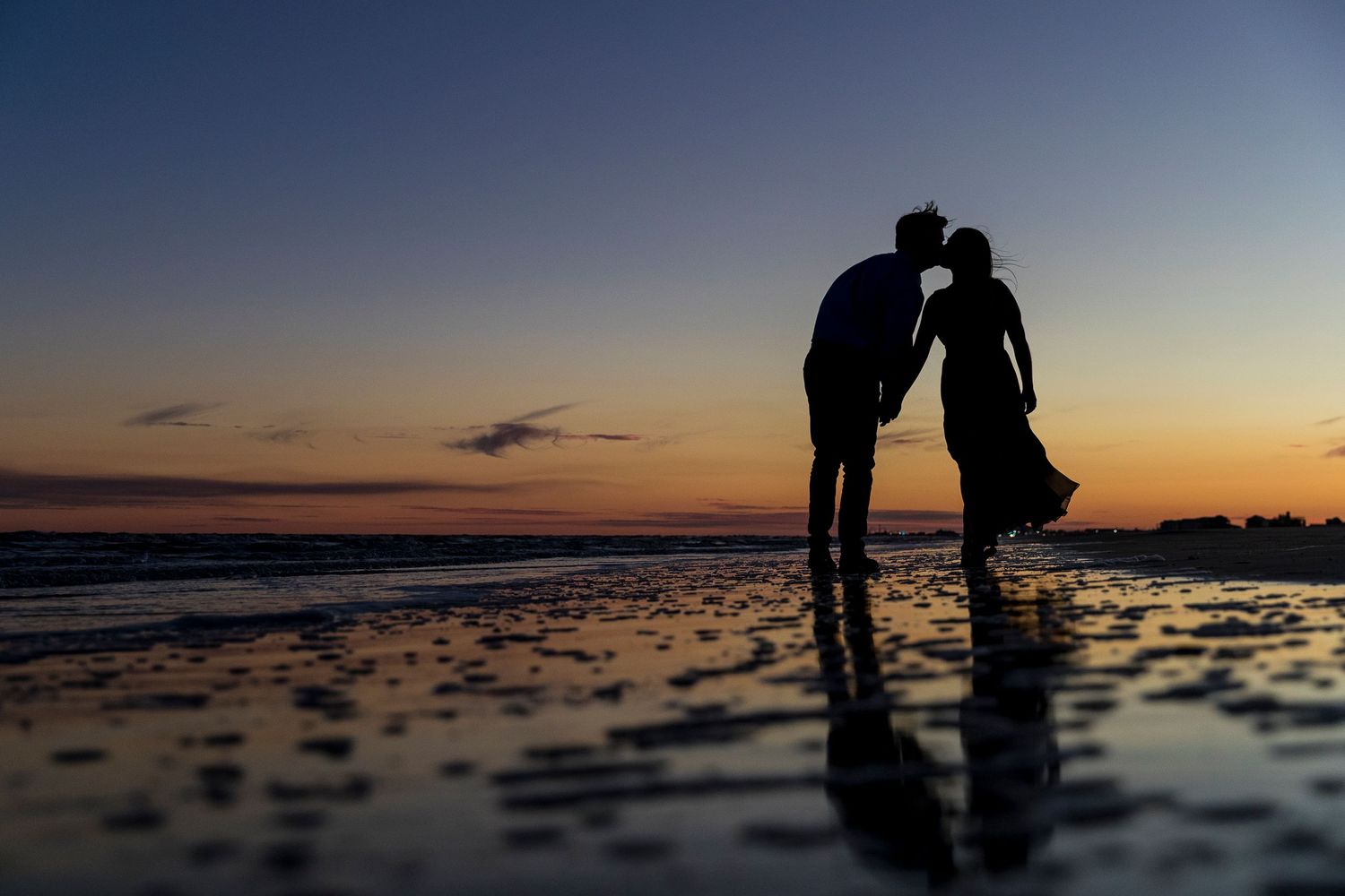 Silhouettes of a couple on beach at sunset creating romantic shadows on wet sand.
