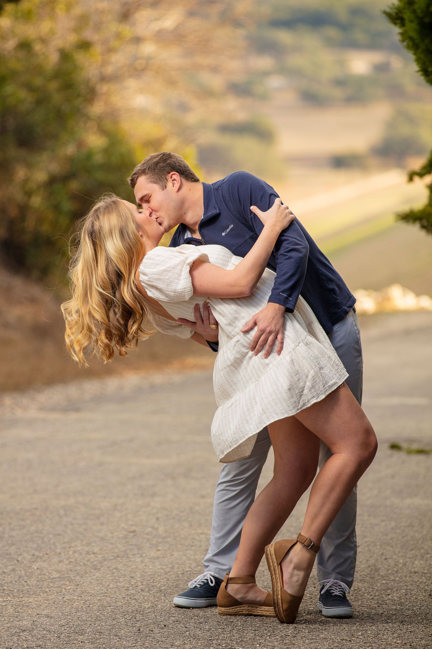 Romantic dip kiss sequence between couple on outdoor path with scenic background.