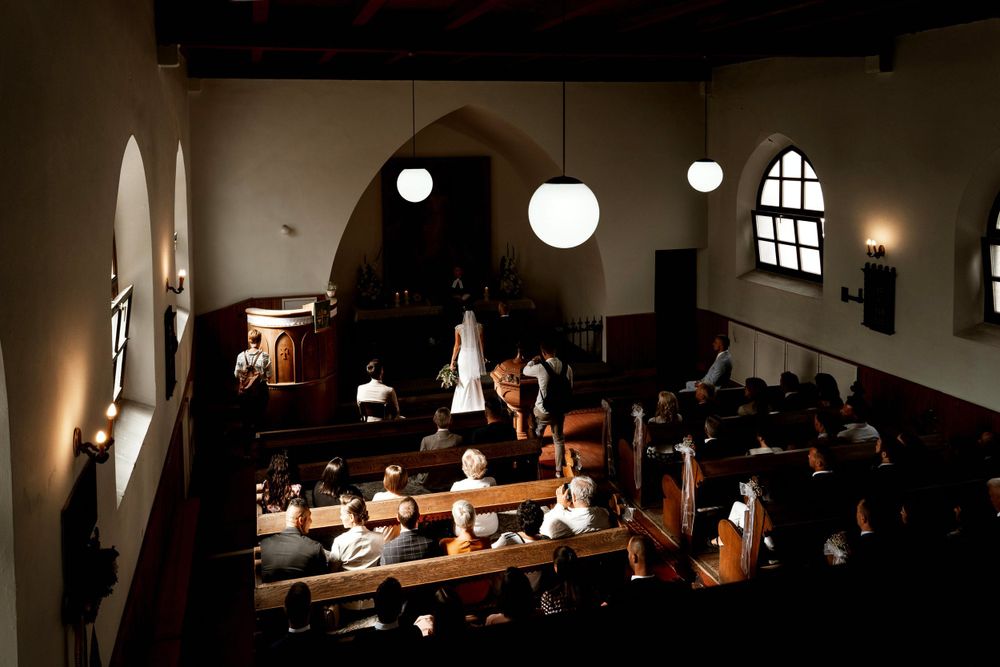 Church wedding ceremony in progress with natural light streaming through arched windows.
