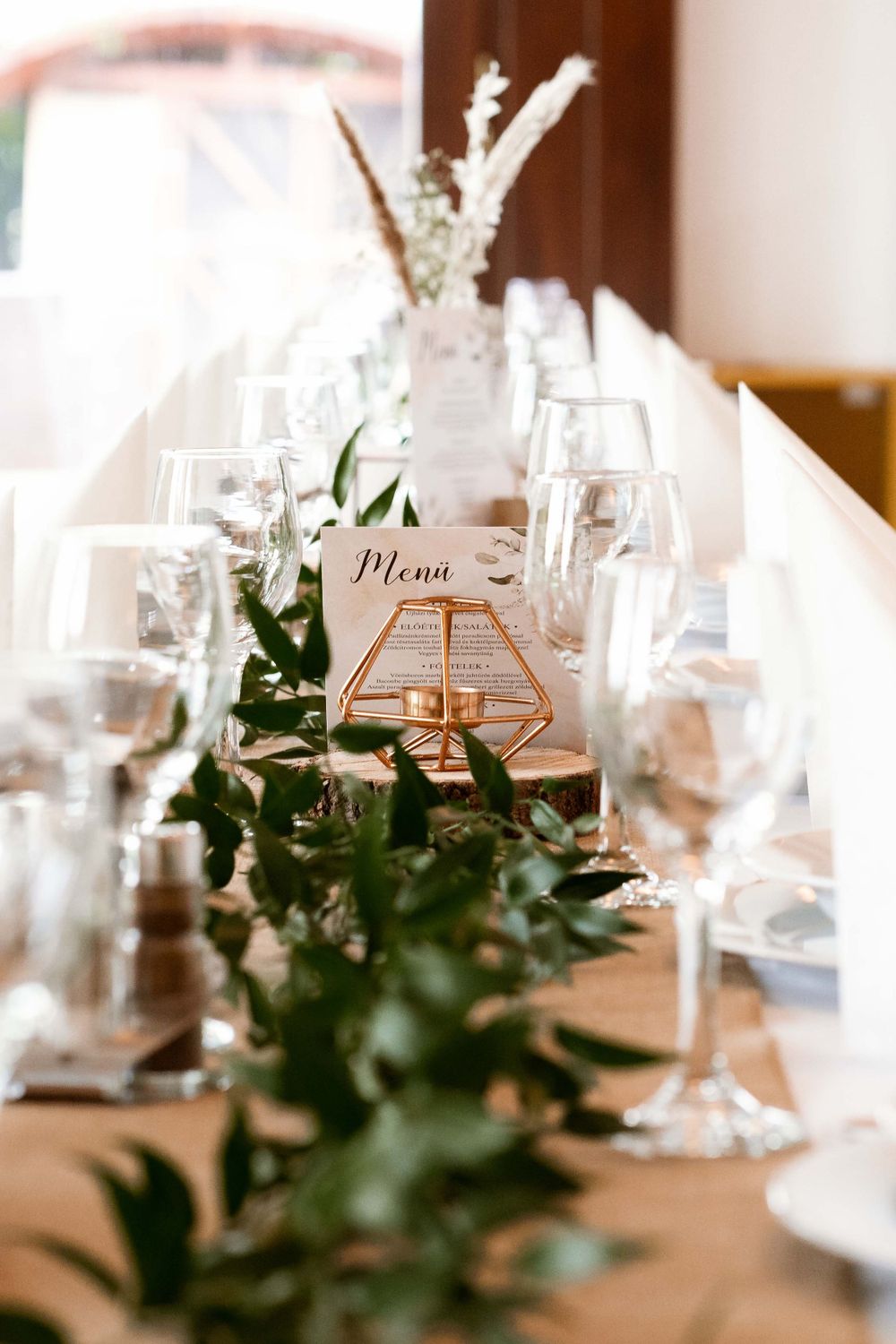 Elegant wedding table setting with menu card, greenery and geometric gold centerpiece.