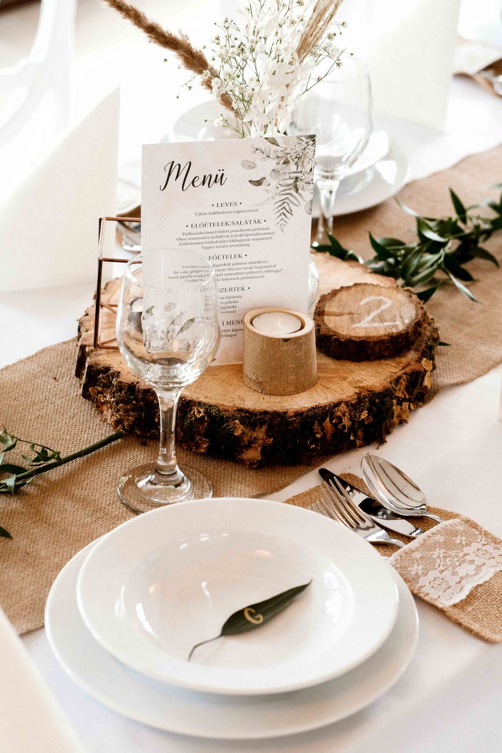 Rustic wedding table setting with menu card on wood slice, burlap runner and white flowers.