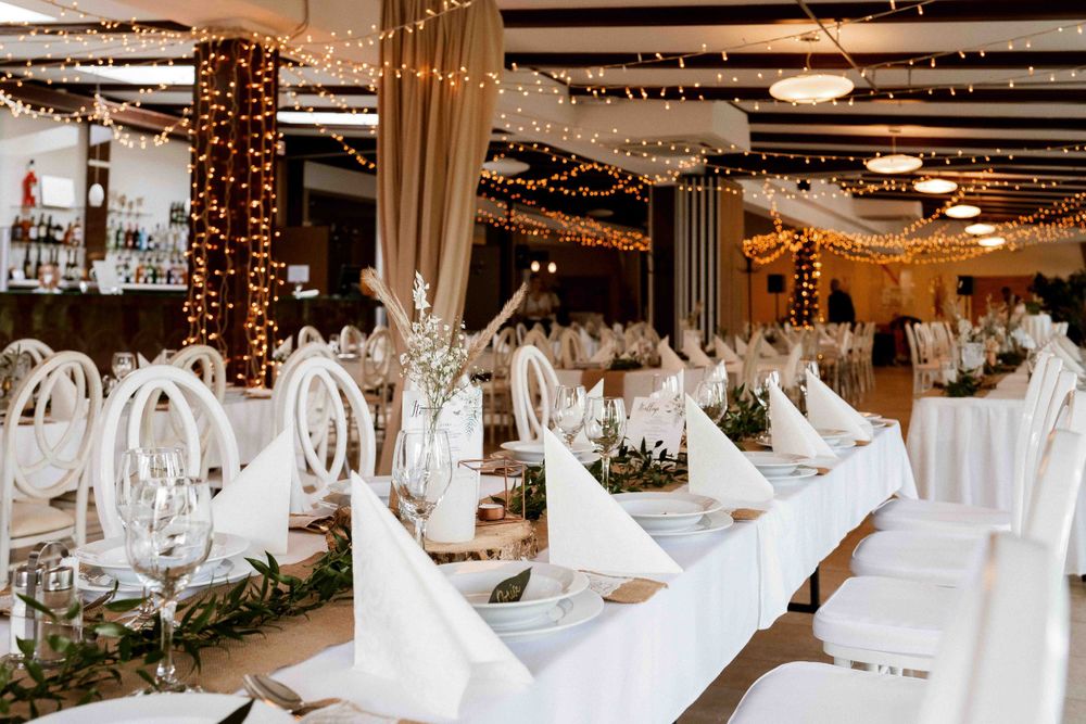 Elegant wedding reception venue with white table settings and twinkle lights decorating pillars.
