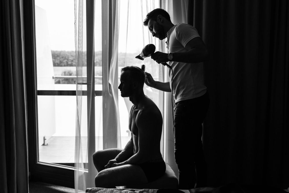 Black and white image of wedding preparation by window with dramatic lighting.