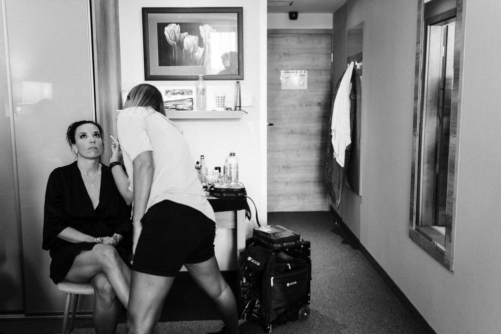 Two people relax in a hallway with luggage and framed artwork visible.
