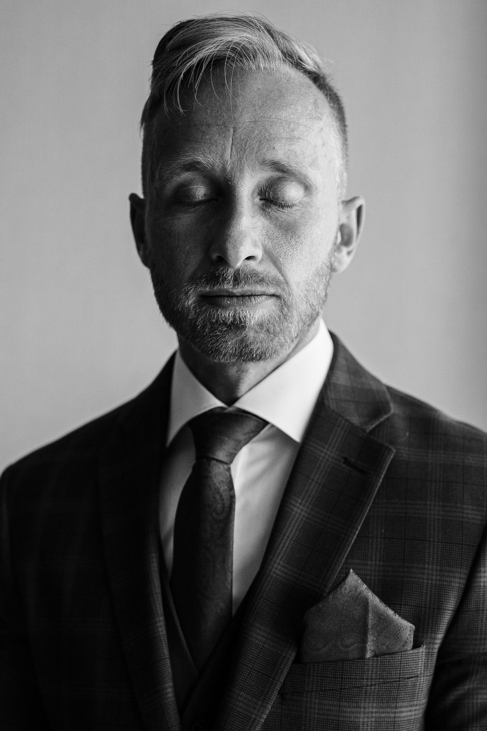 Close up portrait of man in suit with eyes closed against neutral background.