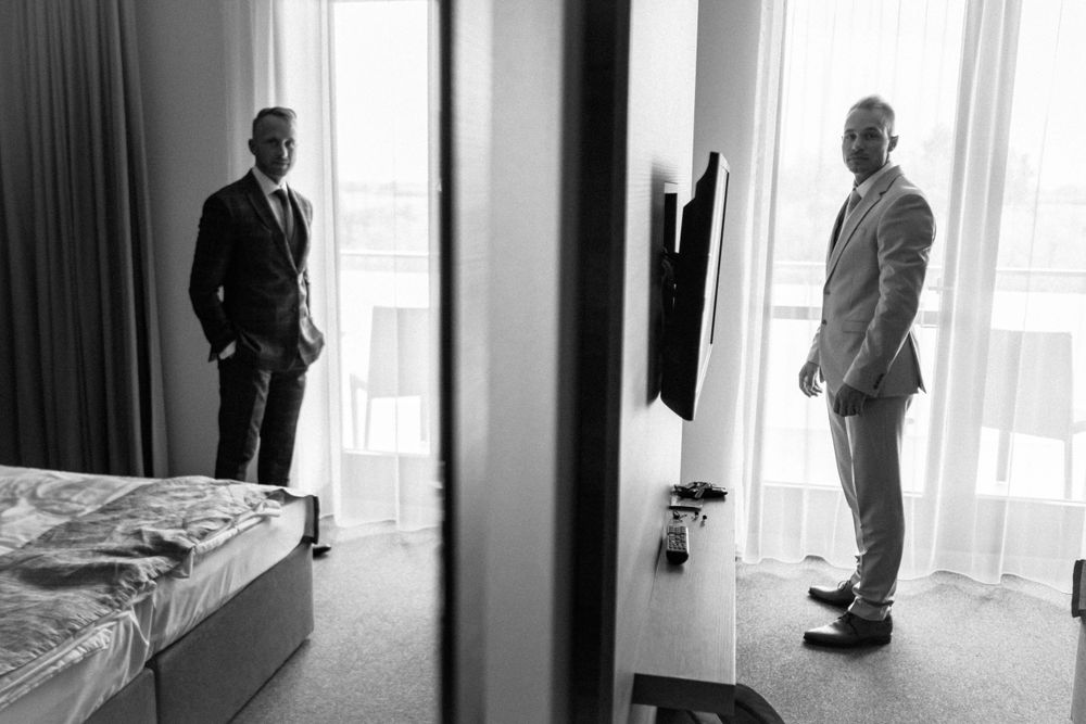 Black and white photo shows two men in suits standing in separate hotel rooms.