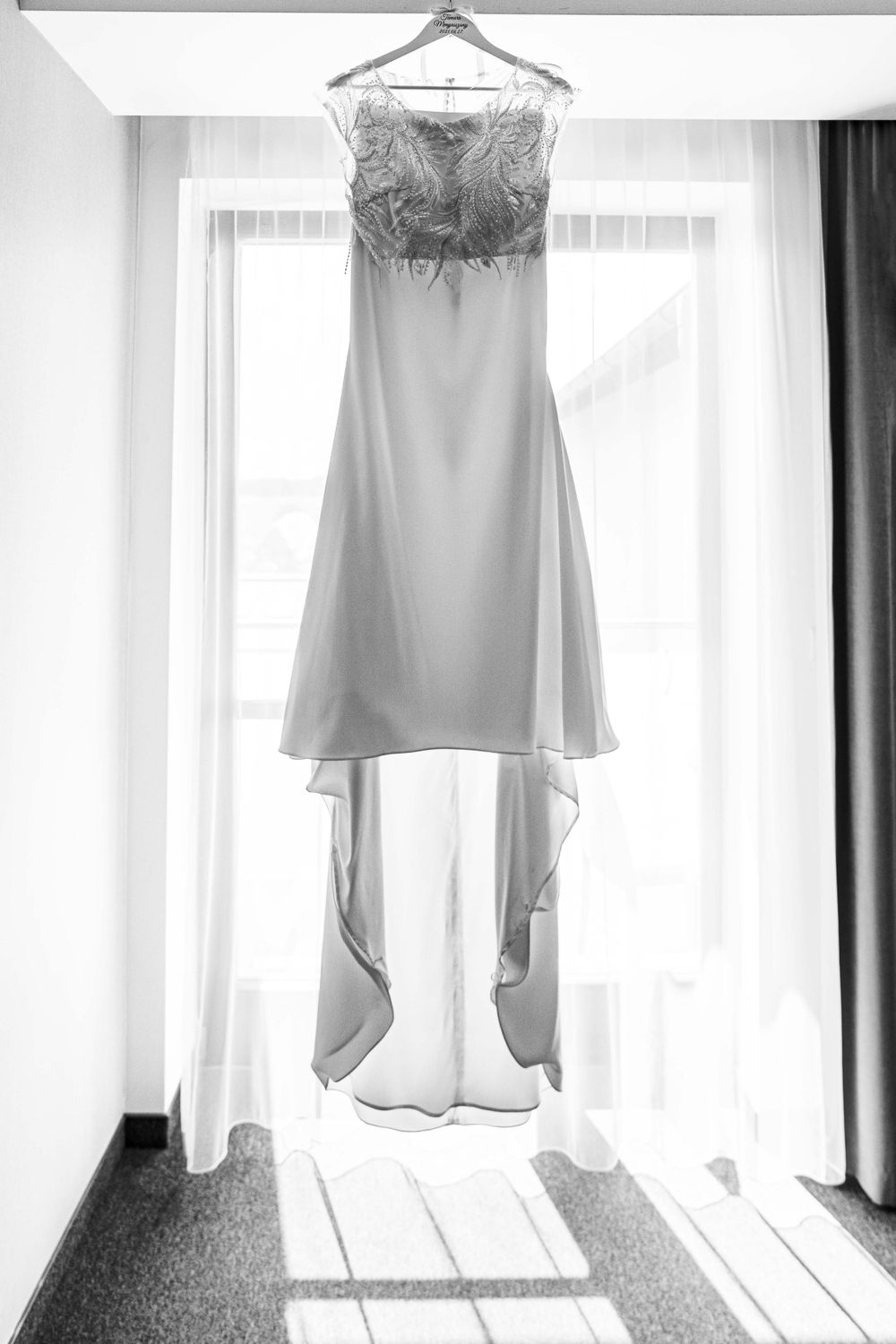 White wedding dress hangs elegantly against bright window with flowing train.