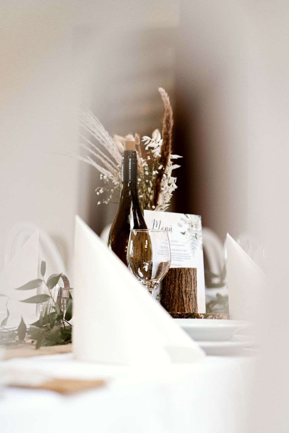 Minimalist wedding table setting with dried flowers and white linens in soft focus.