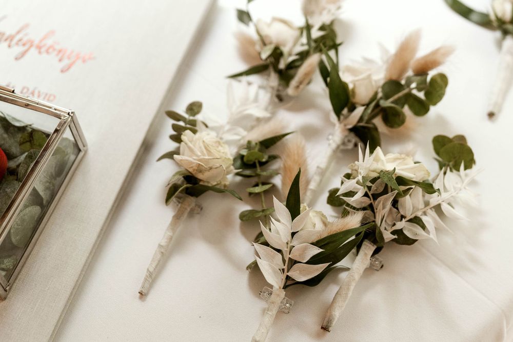 Delicate white and cream wedding boutonnieres with greenery arranged on a light surface.