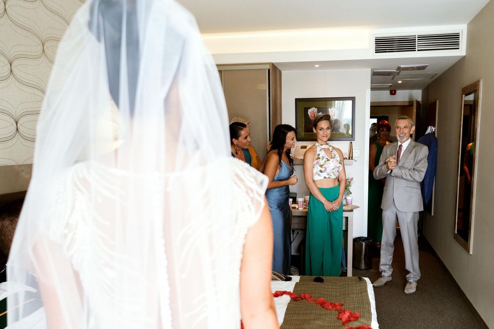 Wedding party members in formal attire gather in a hotel hallway for first look reactions.