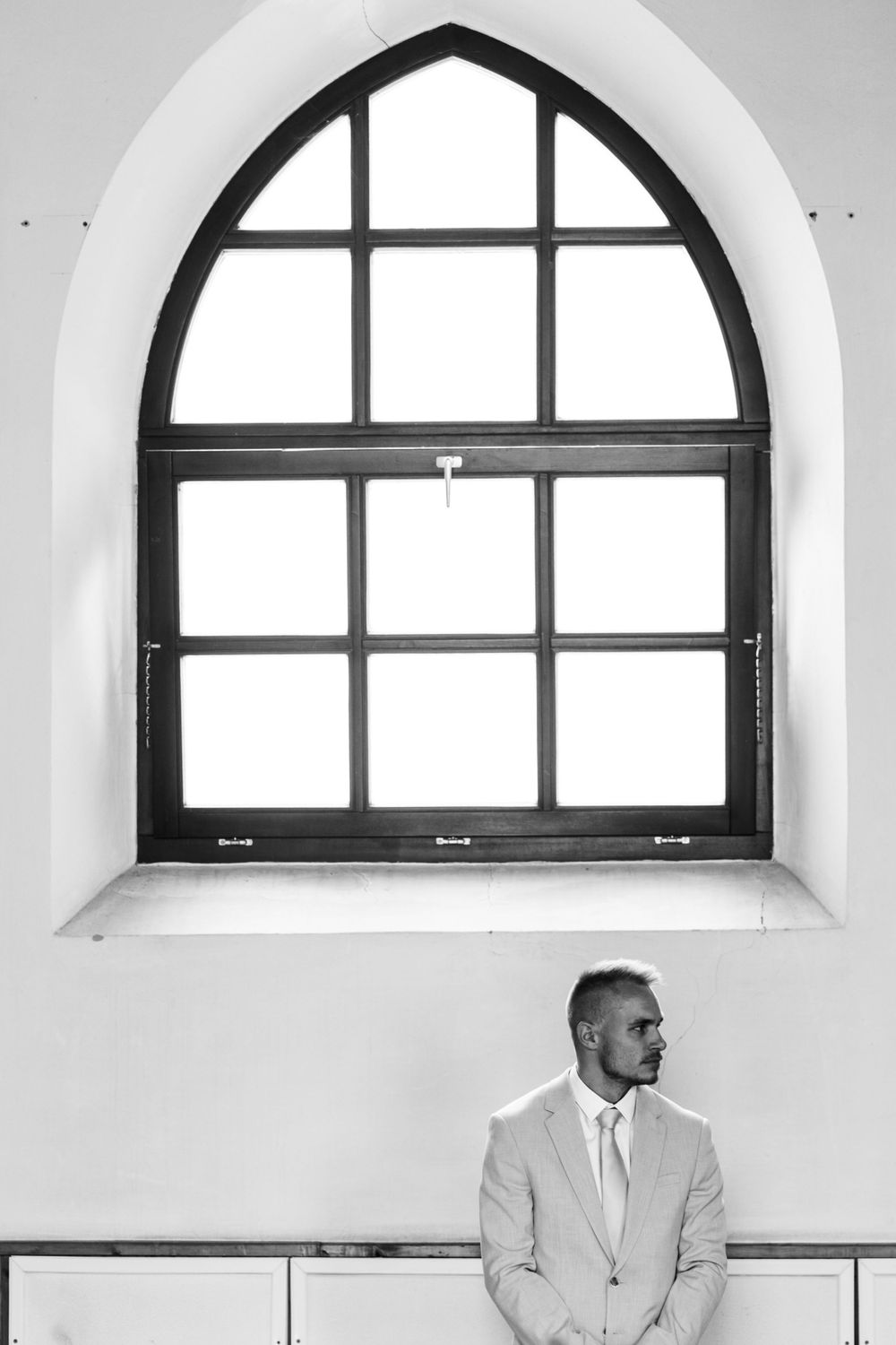 Minimalist black and white architectural photo of an arched church window with figure below.