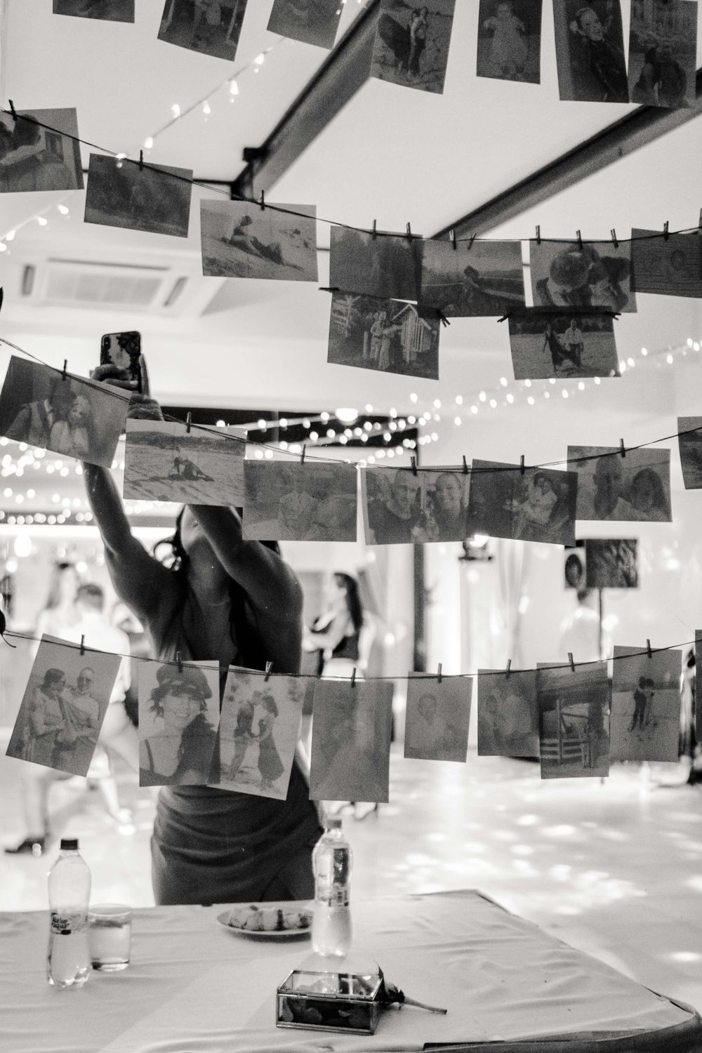 Vintage photographs hanging on strings with fairy lights creating an artistic display at an event.