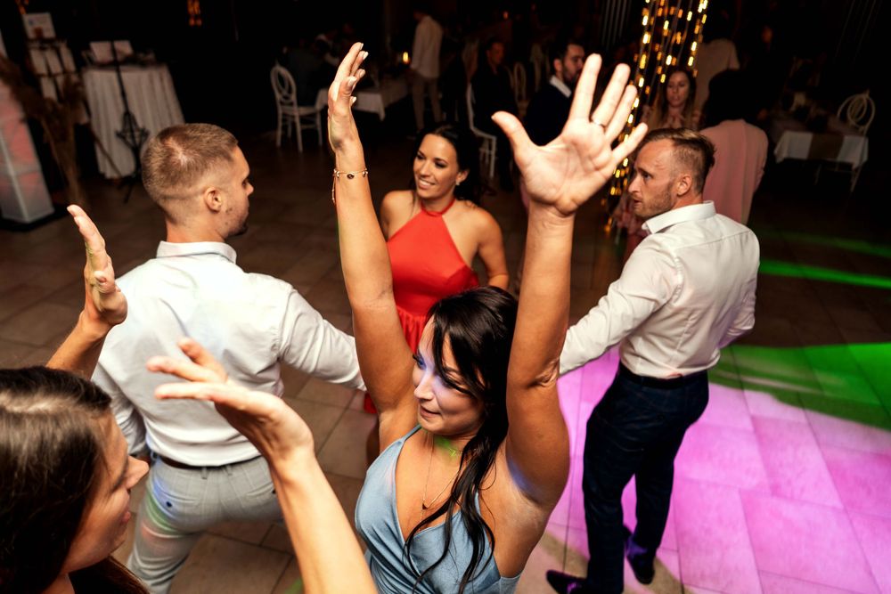 Energetic crowd dancing and raising hands on a colorfully lit dance floor.