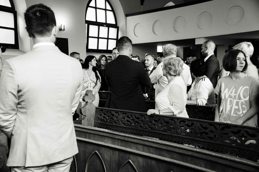 Black and white photo of wedding guests standing in church pews during ceremony.