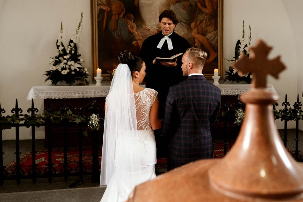 A wedding ceremony taking place in a church with an officiant and couple at the altar.