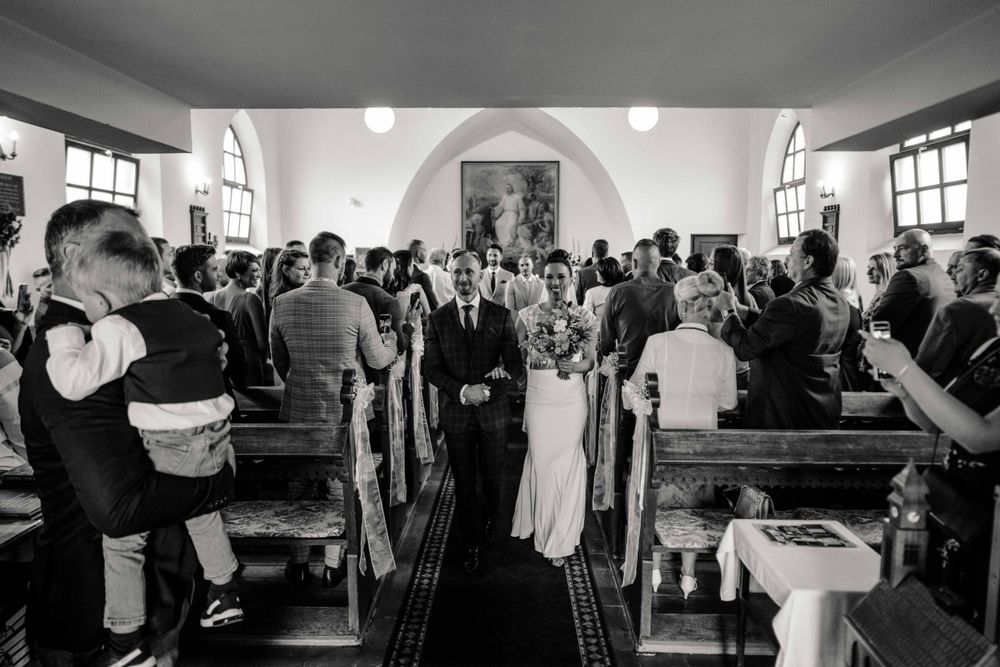 Black and white photo of wedding ceremony with guests standing in church pews.