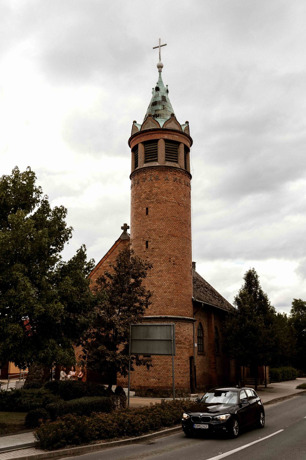 A brick church with a distinctive tower and cross under cloudy skies.