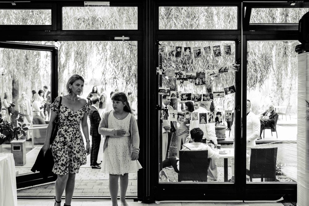 Black and white photo of people looking at photo displays through window glass.